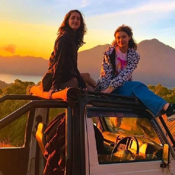 Friends sitting on top of classic 4x4 safari jeep roll bar during golden sunrise in Kintamani Bali