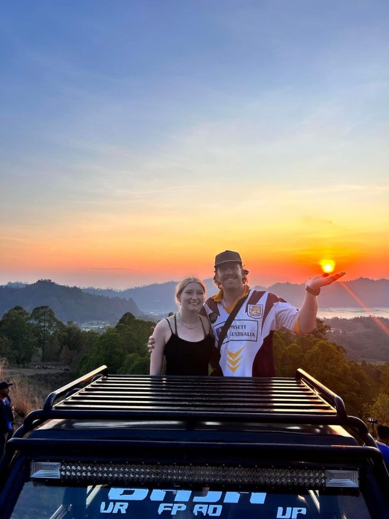 Couple standing on 4x4 safari jeep holding golden sunrise sun over Mount Batur volcano