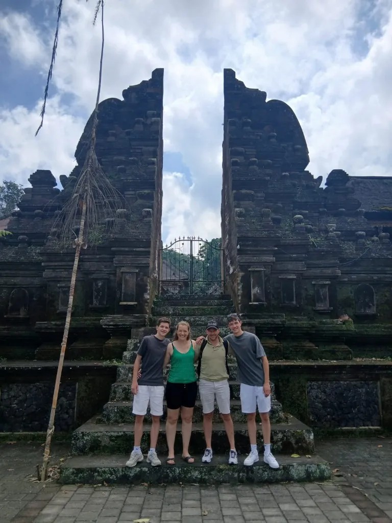 Tour guide and riders exploring an ancient Balinese stone temple entrance surrounded by tropical banyan trees